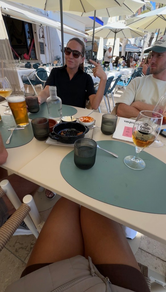 A group of people at a restaurant table with drinks, discussing and enjoying food outdoors under umbrellas.